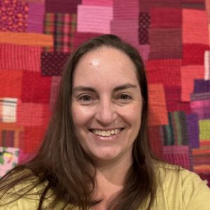 Jen Strauser, smiling in front of a Kawandi style quilt